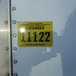 A yellow New Jersey DEP solid waste transporter license sticker, numbered 11122 and expiring June 30, 2013, is affixed to a white metal surface—commonly seen on vehicles for junk removal in Morris County NJ.