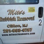 The side of a vehicle displays "Mike's Rubbish Removal, Clifton, NJ, 201-803-0787, www.mitoscleanouts.com," advertising junk removal in Passaic County NJ, with a yellow sticker labeled "11123" next to the door handle.