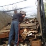 A person stands in the back of a truck filled with discarded items and debris, lifting a rolled-up carpet among piles of materials and furniture—capturing a typical day of junk removal in Bergen County NJ.