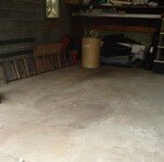 A mostly empty garage with a bare concrete floor, a wooden chest, ladder, and storage items against the walls—ideal for anyone seeking junk removal in Passaic County NJ to clear out and reclaim their space. Shelves and boxes sit in the background.