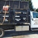 A black and white junk removal truck is parked outdoors in Essex County NJ. The side of the truck displays services such as attic, basement, garage, pool removal, and a phone number, with the company logo visible on the door.